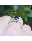 white gold ring underside with a blue sapphire gemstone on a finger against a green leafy background