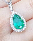 Teardrop-shaped emerald pendant on a white gold chain held between fingers.