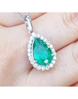 Teardrop-shaped emerald pendant on a white gold chain held between fingers.