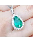 Pear-shaped deep green emerald pendant with diamond halo, set in 18K white gold.
