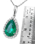 Emerald green teardrop pendant with chain next to a ruler for size reference