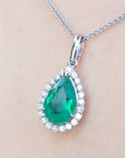 Emerald teardrop pendant with diamond accents on a beige skin background