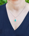 A woman wearing a necklace with a natural colombian emerald pendant against a natural background