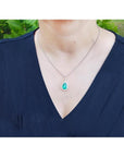 18K white gold pear-shaped emerald pendant with diamond halo on a woman's neck.