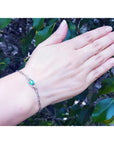 14K white gold paper clip bracelet with a bluish-green emerald and diamond halo on a woman's wrist.
