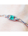 A paper clip bracelet style whit a halo natural diamond surrounding a genuine colombian emerald on a wrist.