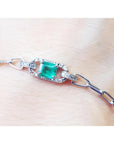 A paper clip bracelet style whit a halo natural diamond surrounding a genuine colombian emerald on a wrist.