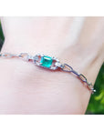 14K white gold paper clip bracelet with a rectangular bluish-green emerald and diamond halo on a wrist.