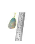 Ethiopian opal pendant with gold setting next to a ruler on a white background