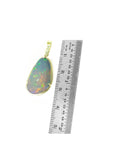 Ethiopian opal pendant with gold setting next to a ruler on a white background