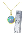 Opal pendant necklace with gold chain next to a ruler for scale on a white background.