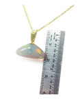 Opal pendant on a gold chain with a ruler for scale on a white background