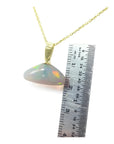 Ethiopian Welo opal pendant with full play of colors, 14k gold bail, and chain next to a ruler.