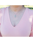 Person wearing a light pink top with an opal pendant necklace outdoors.