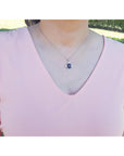 A woman wearing a pink blouse with a necklace featuring a black opal pendant outdoors.