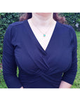 Woman wearing a navy blue dress and an Asscher cut emerald necklace pendant with a blurred green background