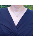 Navy blue top worn by a woman with an emerald necklace against a blurred green leafy background