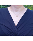 Oval cut emerald and natural diamond pendant necklace on a 14K yellow gold chain, worn on a model.