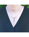 Yellow gold necklace with natural emeralds on a woman collar wearing a dark green top against a blurred green background