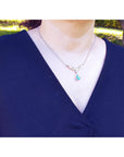 Woman wearing a blue top with a necklace featuring a dangling natural teardrop emerald pendant outdoors.