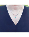 A lady wearing a blue dress with a white gold pear cut emerald necklace featuring a halo diamond pendant.