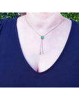 Emerald lariat necklace with an emerald-cut natural emerald, milgrain, prongs, and dangling pearls on a gold box chain.