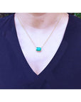 Authentic Colombian Emerald necklace rectangular emerald-cut worn by a woman in a navy blue top.