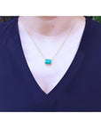 Emerald-cut Colombian emerald solitaire necklace in 18K yellow gold on a woman's chest.