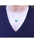 Emerald-cut Colombian emerald solitaire necklace in 18K yellow gold on a woman's chest. styled with a black V-neck top.