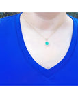 Emerald-cut Colombian emerald pendant with diamond halo on 14k yellow gold chain, worn on a blue shirt.