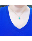 Emerald-cut Colombian emerald pendant with diamond halo on 14k yellow gold chain, worn on a blue shirt.