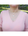 White Ethiopian opal pendant in 14K yellow gold, worn on a woman's neck over a pink shirt.