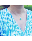 Person wearing a blue and white patterned top with a necklace featuring a Welo opal gold pendant. pendant.