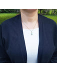 Person wearing a navy cardigan over a white shirt with an Ethiopian opal pendant on a blurred green outdoor background.