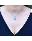 Emerald necklace with halo natural diamonds on a 14K yellow gold chain, worn on a woman's neck.