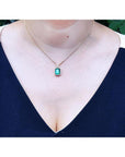 Emerald necklace with halo natural diamonds on a 14K yellow gold chain, worn on a woman's neck.