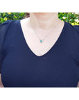 Woman wearing a navy blue top with a horseshoe emerald necklace against a green outdoor background