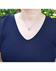 Woman wearing a 14K white gold horseshoe necklace with a green oval emerald and diamonds.