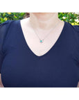 Woman wearing a 14K white gold horseshoe necklace with a green oval emerald and diamonds.