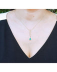 14K yellow gold twisted slider necklace with a pear-shaped Colombian emerald pendant on a woman's neck.