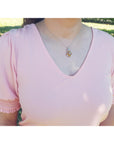 A woman wearing a pink blouse with ruffled sleeves and an opal silver pendant necklace outdoors.