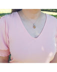 A woman wearing a pink blouse with ruffled sleeves and an opal silver pendant necklace outdoors.