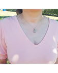 Person wearing a pink blouse with a silver opal necklace against a blurred natural background.