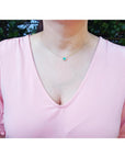 Oval Muzo emerald necklace in 14K yellow gold, worn on a woman in a pink top.