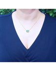 Woman wearing an 18K yellow gold necklace with a bezel-set, east-west emerald-cut bluish-green emerald.