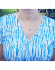 Person wearing a blue and white patterned shirt with an Ethiopian opal pendant necklace outdoors.