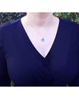 Tilted heart emerald necklace with halo diamonds in 18K yellow gold, worn on a model.