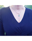Woman wearing a blue dress with a white gold necklace featuring a natural emerald pendant against a grassy background