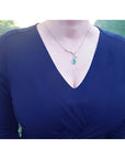 Pear cut natural emerald necklace with diamond halo in 18K white gold, worn on a dark blue dress.