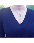 Pear cut natural emerald necklace with diamond halo in 18K white gold, worn on a dark blue dress.